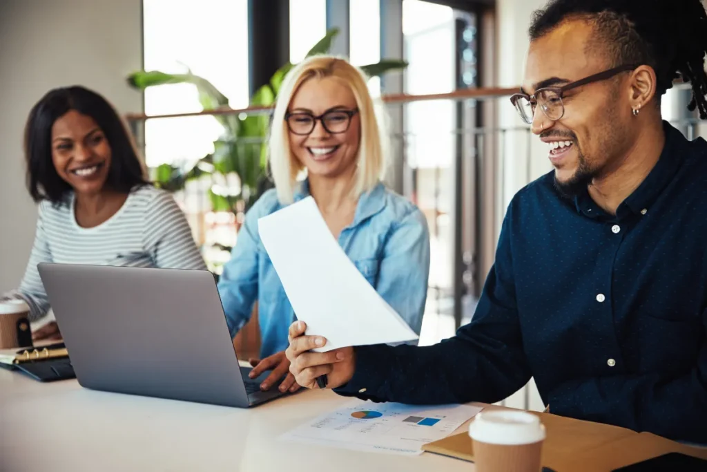 Colleagues laughing while reviewing laptop and documents