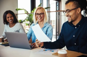 Colleagues laughing while reviewing laptop and documents