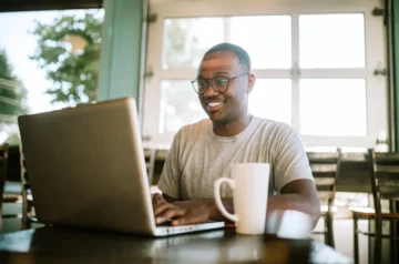 Man smiling while working on laptop at a cafe